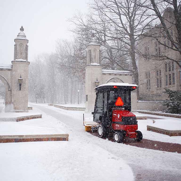A small vehicle with a snowplow clears snow from in front of the Sample Gates.