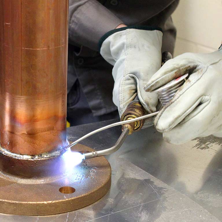 A person solders a copper pipe fitting.
