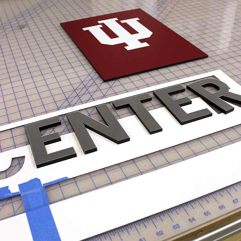 The IU trident and letter cutouts form the word 'Enter' arranged on a cutting mat